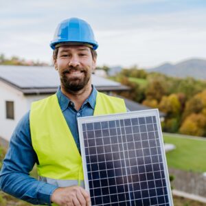 Smiling handyman solar installer standying with solar module while installing solar panel system on